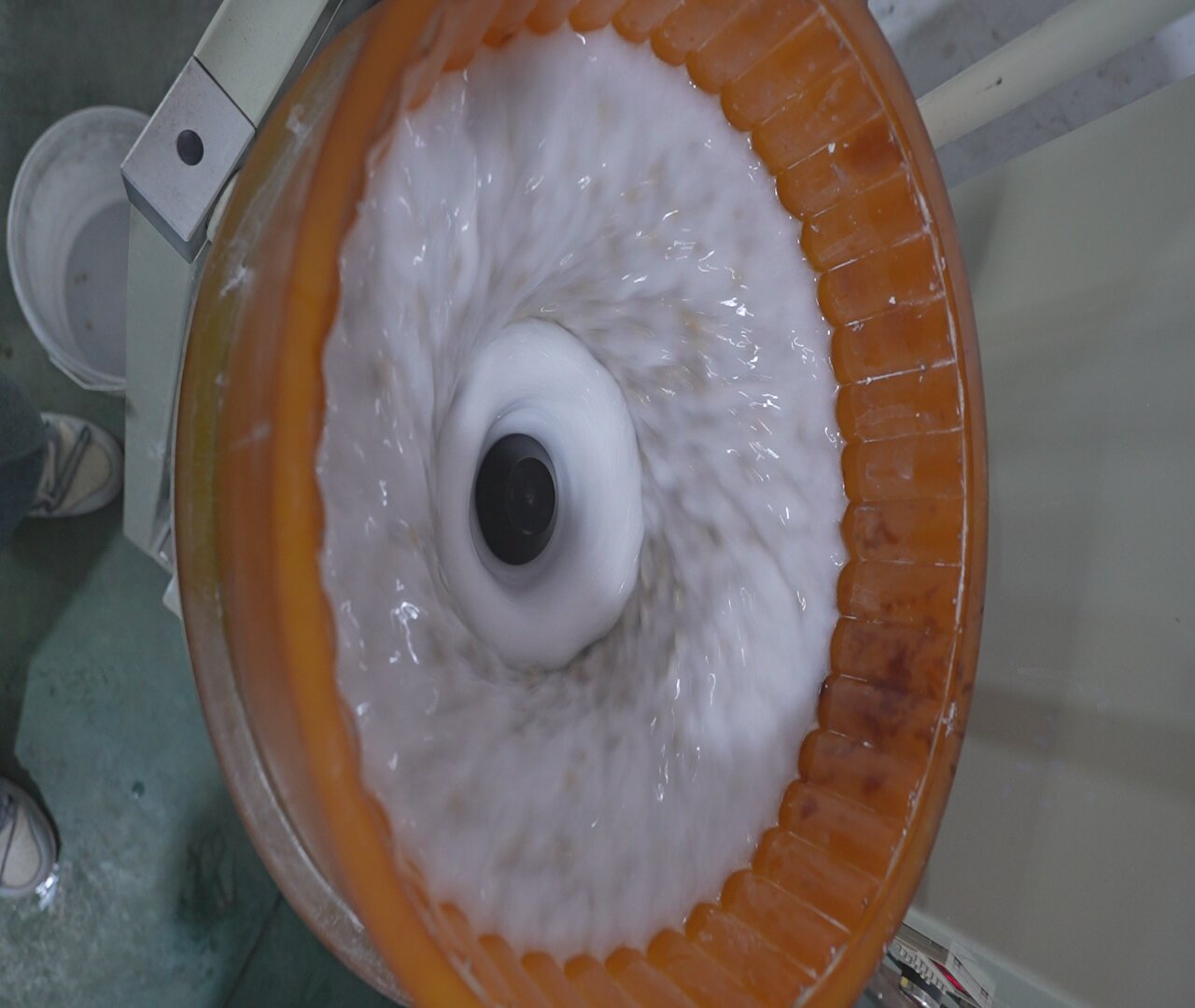 Interno di una macchina a tazza in funzione: rivestimento in poliuretano arancione, acqua e media in flusso toroidale attorno al mozzo centrale